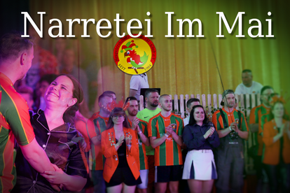 Gruppe von Menschen in orange-grünen Trikots und anderen Kleidungsstücken vor grünem Hintergrund mit dem Text 'Narretie Im Mai' und einem runden Logo mit einem bunten Narrenkopf